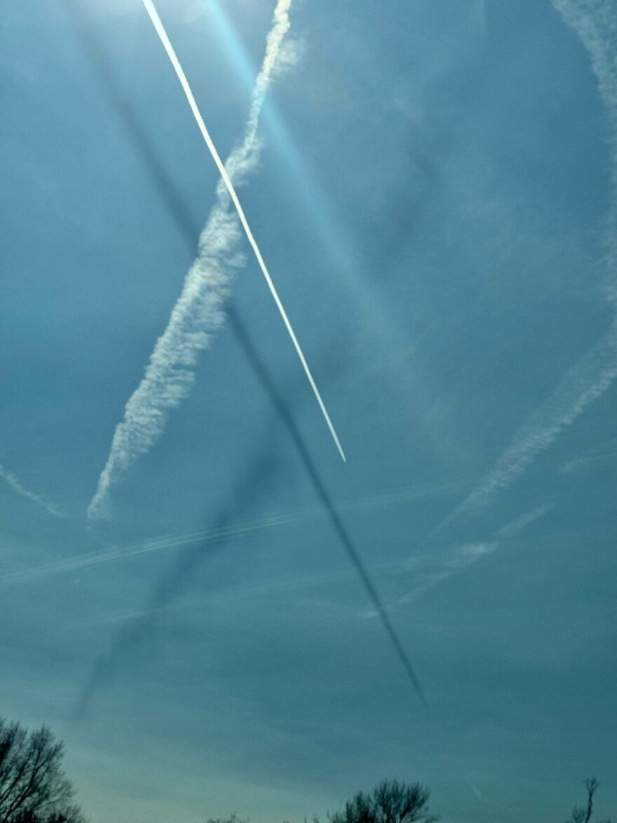 Strange things happening on Earth: Contrails forming an X in the blue sky, with the sun's glare creating bright lines.