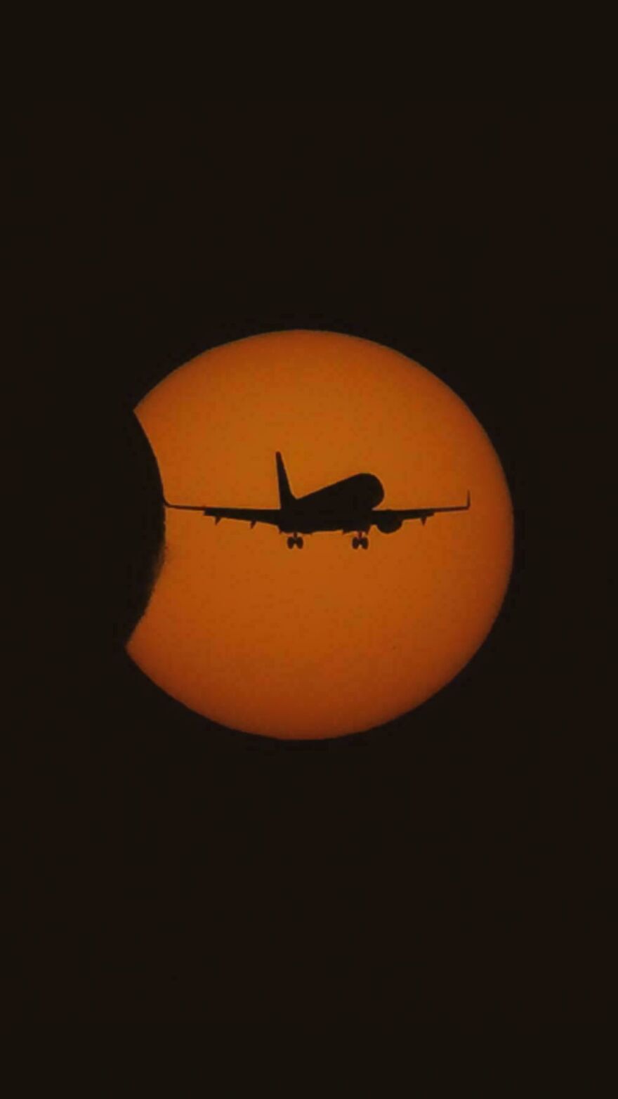 A silhouetted airplane flying in front of a partial solar eclipse, one of many incredible things happening on Earth.