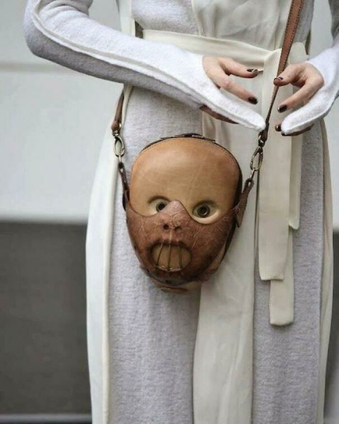 A woman carries a purse shaped like a baby doll head with a Hannibal Lecter-style mask, a bad fashion crime.