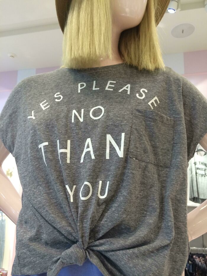 A mannequin wearing a grey T-shirt with the hilariously bad fashion crime text Yes Please No Than You.