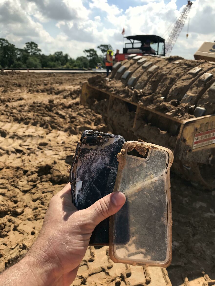 A hand holds two broken, muddy phones, a funny regret after a construction site fail.