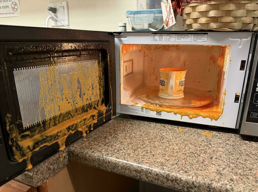 An open microwave with a huge mess of exploded orange food inside and dripping out, a funny unfortunate fail.