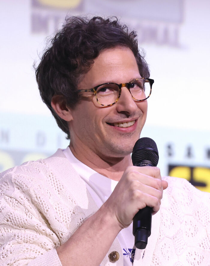 Andy Samberg smiling at a microphone, showcasing his career highlights and bio.
