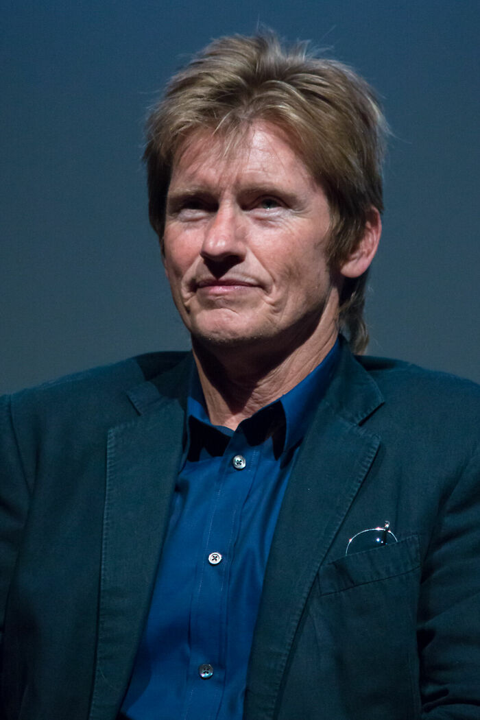 Denis Leary, with a serious expression, in a dark suit and blue shirt, showcasing his career highlights.