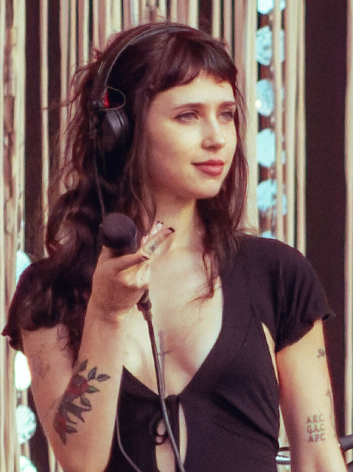 Clairo performing live, wearing headphones and holding a microphone, showcasing her musical career highlights.
