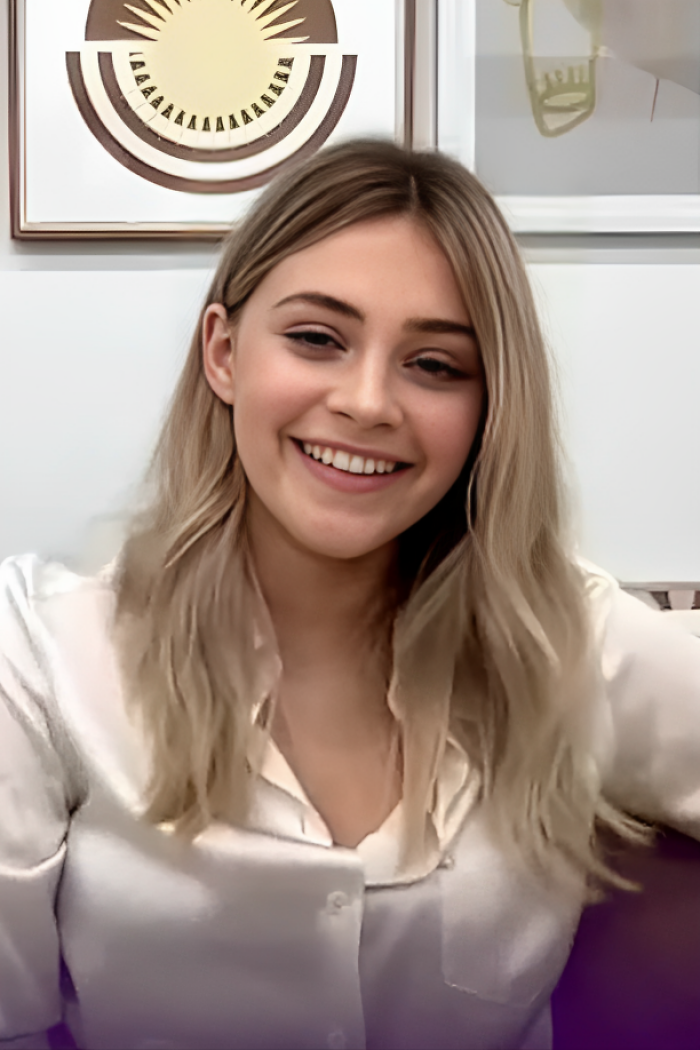 A smiling Josephine Langford with long blonde hair, wearing a light-colored top, highlighting her career.