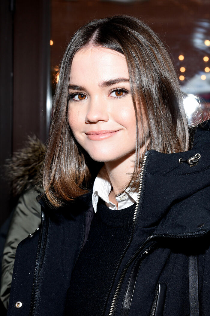 Maia Mitchell career highlights: Young actress with brown hair, smiling in a black winter coat and white shirt.