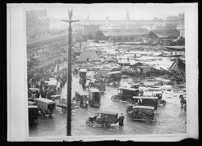 Heartbreaking historical photo showing a street flooded with debris, people, and early 20th-century vehicles.