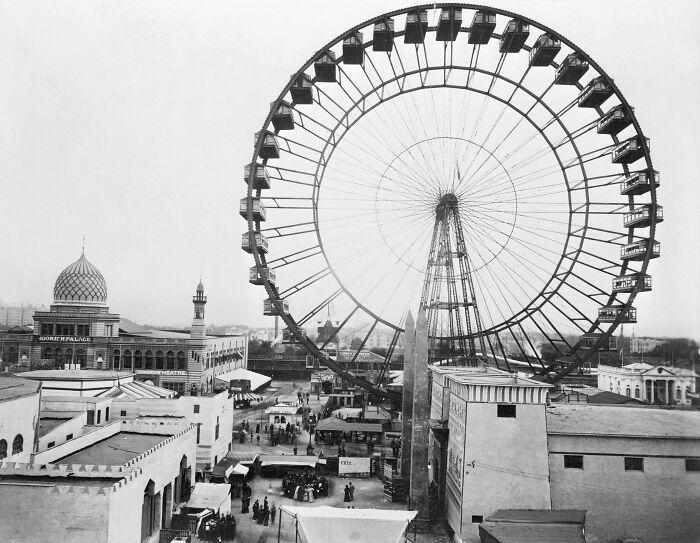 Interesting historical photo of a towering Ferris wheel at a fairground, with buildings and crowds below.