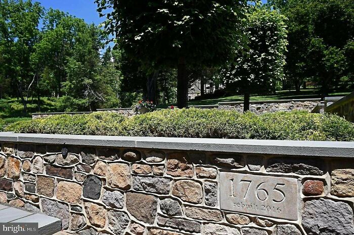 A beautiful historical photo of a stone wall with the numbers 1765 rebuilt 2016 carved into it, amidst lush greenery.
