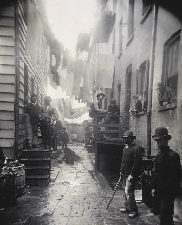 Heartbreaking photo from history of an alleyway with laundry hanging overhead, people standing around, and brick buildings