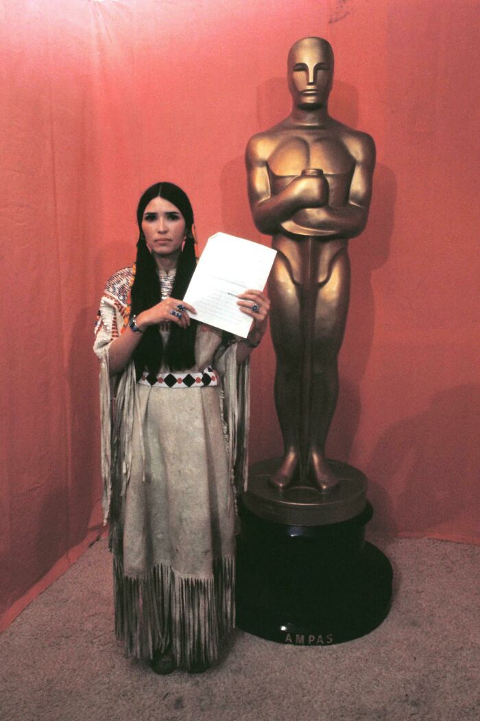 A historical photo of an Indigenous woman with an Oscar statue, holding a speech, an interesting and beautiful moment from history.