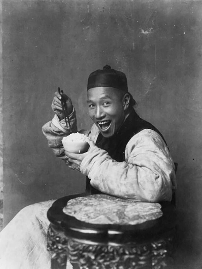 Man with a wide smile, holding a bowl and chopsticks, an interesting historical photo.