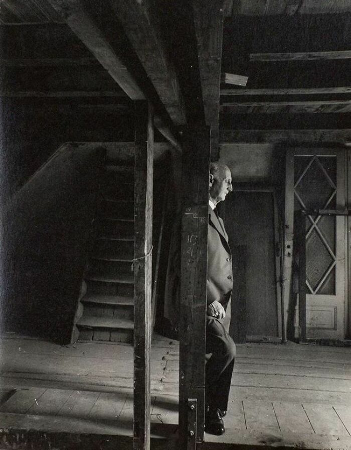 A man in a suit standing in a dimly lit, rustic room with wooden beams, a beautiful photo from history.