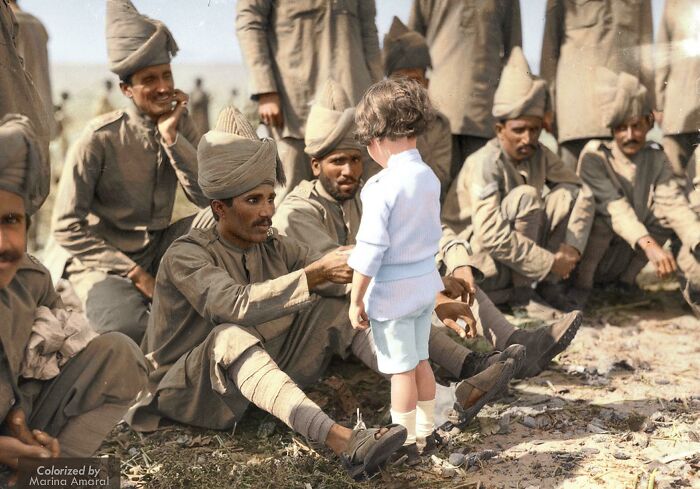 A heartwarming historical photo shows a small child interacting with several uniformed soldiers seated on the ground.