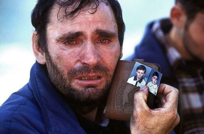 A heartbreaking photo from history of a man crying, holding pictures of two children.