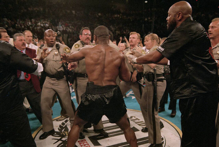 An interesting, heartbreaking photo from history of a boxer being restrained by security guards in a ring.