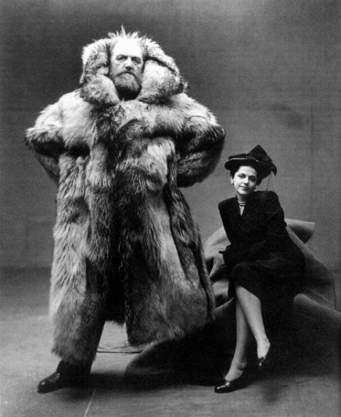 A beautiful, interesting photo from history of a large man in a fur coat standing next to a seated woman.