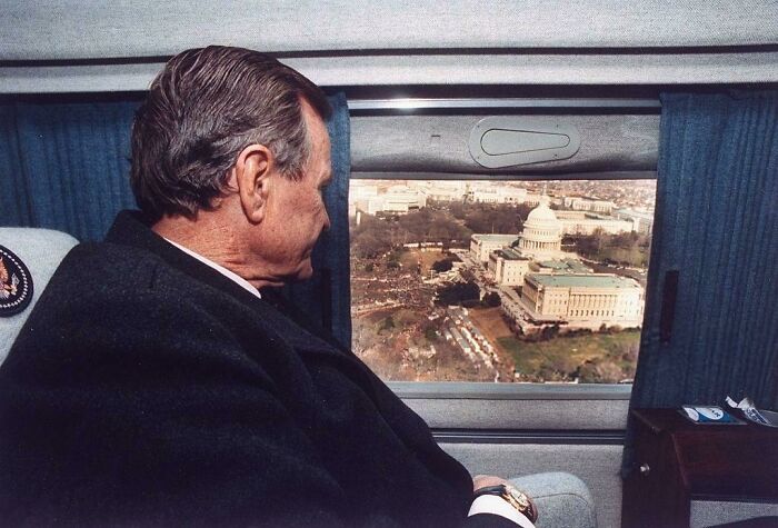 A man looking out a window at the Capitol Building from above, a beautiful and interesting photo from history.
