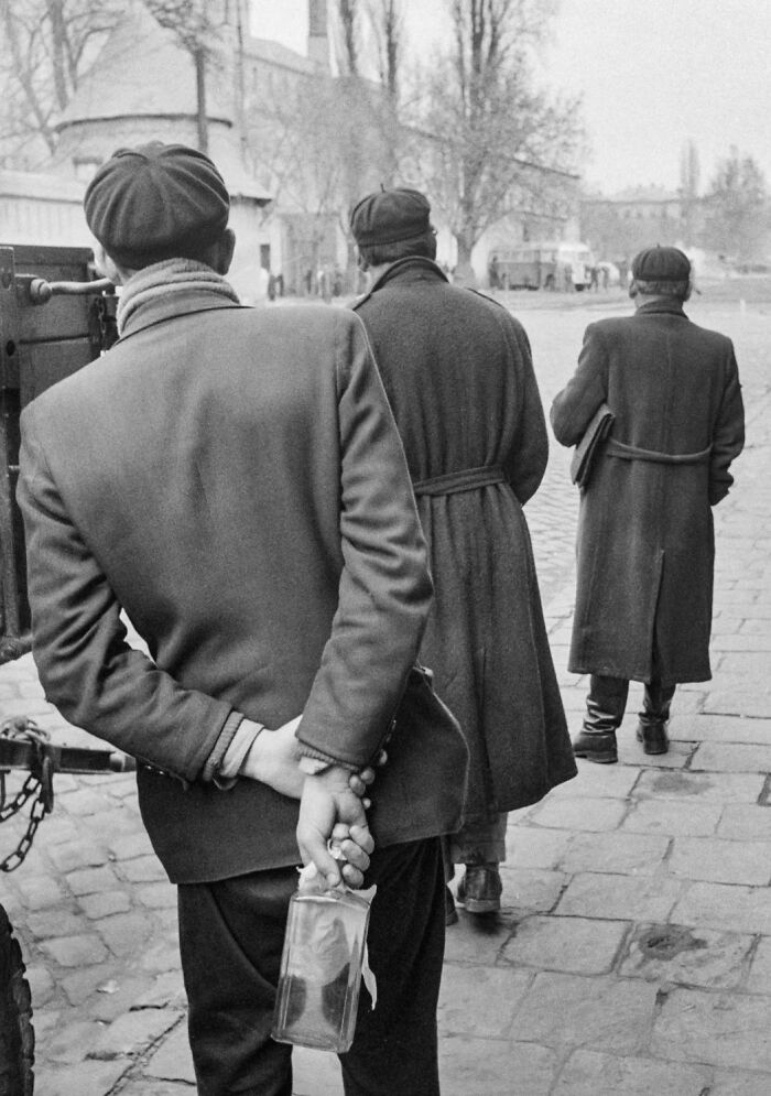 Three men walking away from the camera, one holding a bottle behind his back, a glimpse into history.