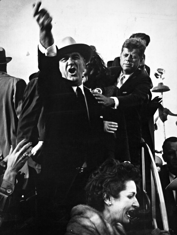 Heartbreaking photo from history showing Lyndon B. Johnson with his arm raised, with John F. Kennedy behind him.