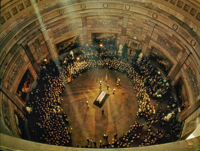 Beautiful photo from history of a casket lying in state in a grand, circular hall, surrounded by many onlookers.