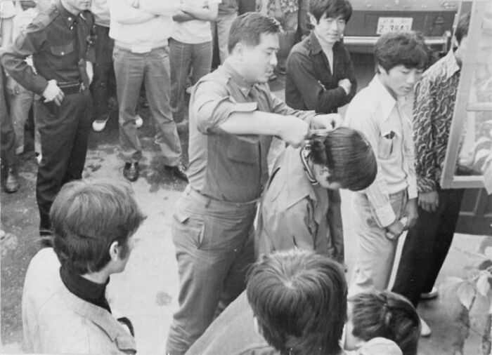 A heartbreaking photo from history shows a man getting his hair cut by another man, surrounded by onlookers.