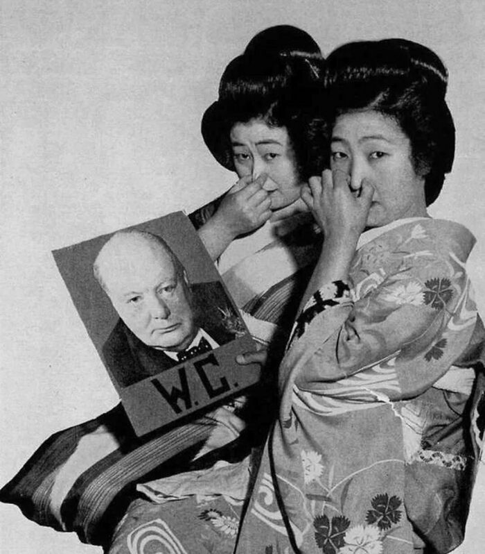 Two Japanese women, with traditional hairstyles, hold a picture of Winston Churchill and pinch their noses in a humorous historical photo.