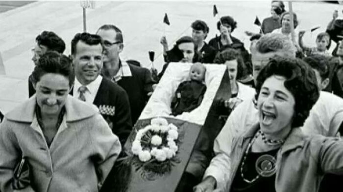 People smile and cheer while carrying a small coffin containing a doll, a curious and beautiful photo from history.