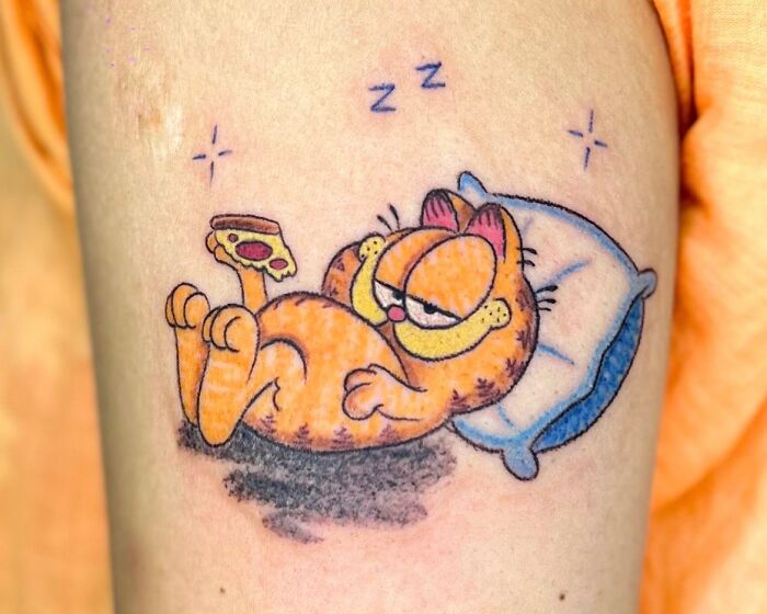 Playful crayon drawing-inspired tattoo of a sleeping Garfield with a slice of pizza, showcasing childhood creativity.