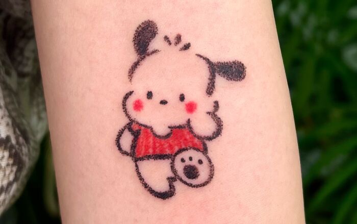 An adorable tattoo resembling a crayon drawing, portraying a cute white dog character with red cheeks and a red shirt, evoking childhood art.