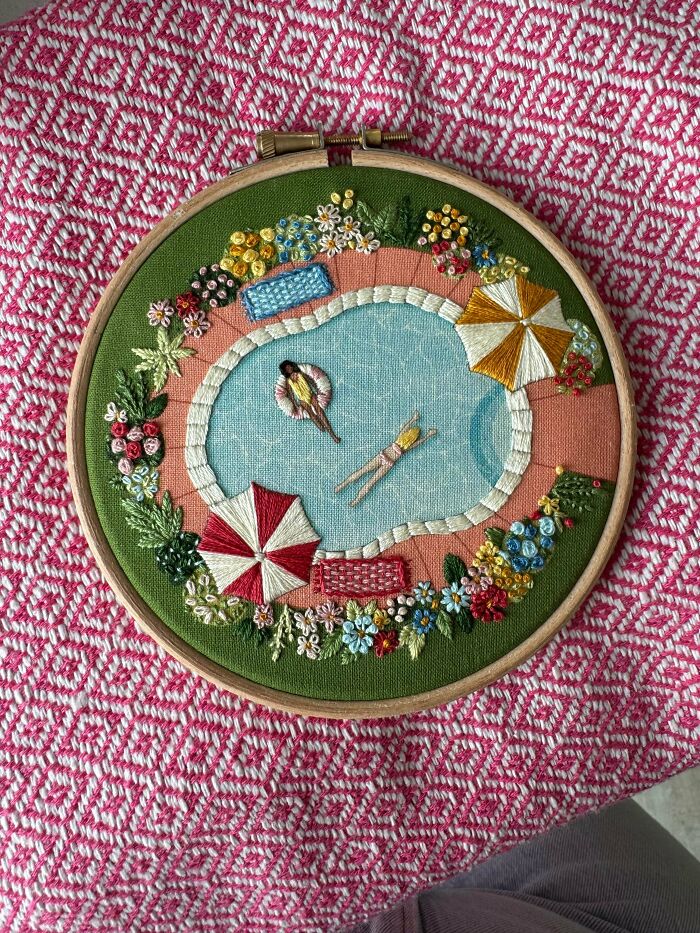 An embroidery hoop art of a swimming pool scene featuring swimmers and umbrellas