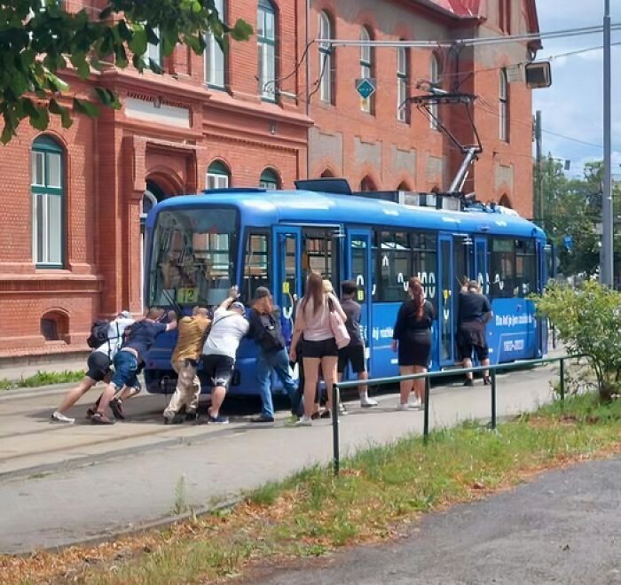 People from Eastern Europe pushing a broken-down blue tram, demonstrating how they are built different.