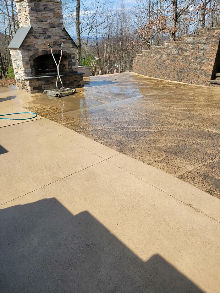 Power washing a large concrete patio next to an outdoor fireplace, revealing clean areas.