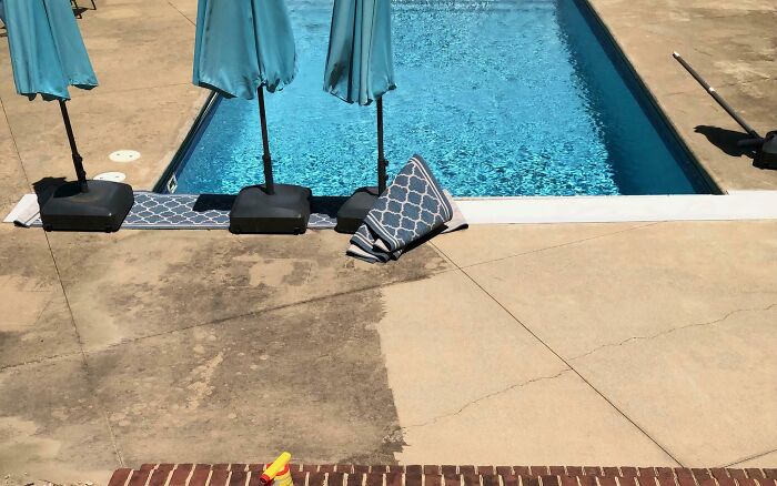Power washing half of a concrete pool deck, showing a satisfying clean contrast.