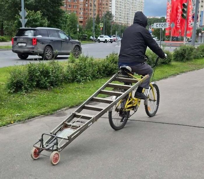Man from Eastern Europe riding a bicycle with an attached long ladder-cart, showcasing how people are built different.