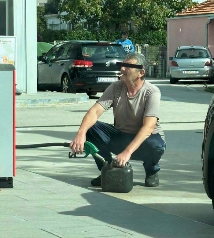 Man from Eastern Europe smoking while filling a jerry can at a gas station, showing how people are built different.