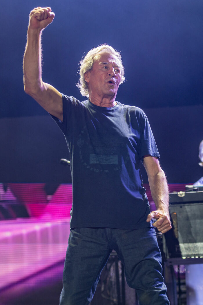 A concert shot of Ian Gillan raising his fist in the air, performing on stage during his career.