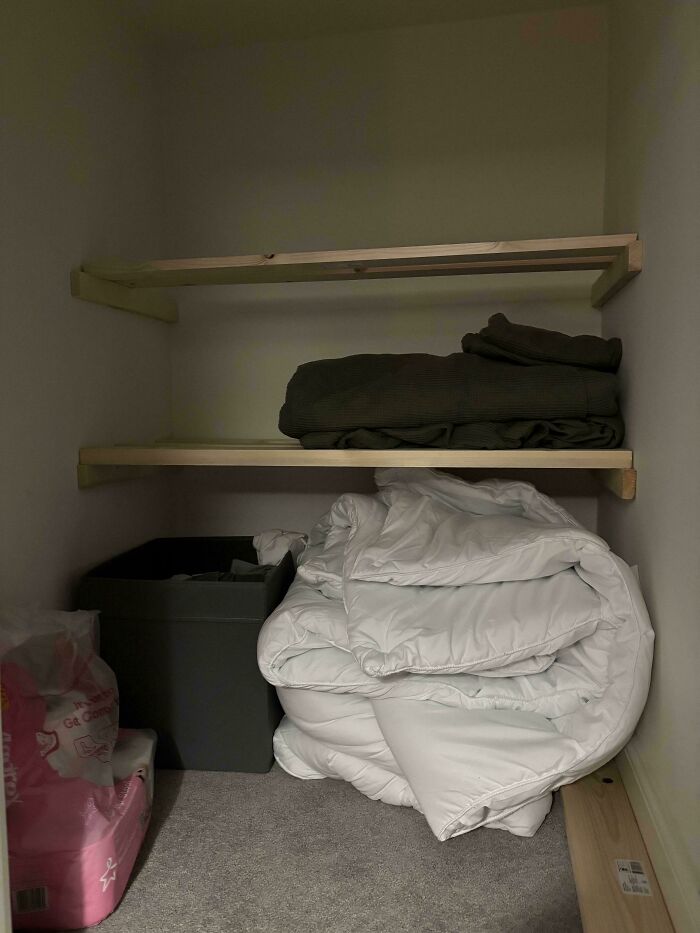Image of a closet with newly installed wooden shelves, featuring folded linens and storage boxes for home renovation.