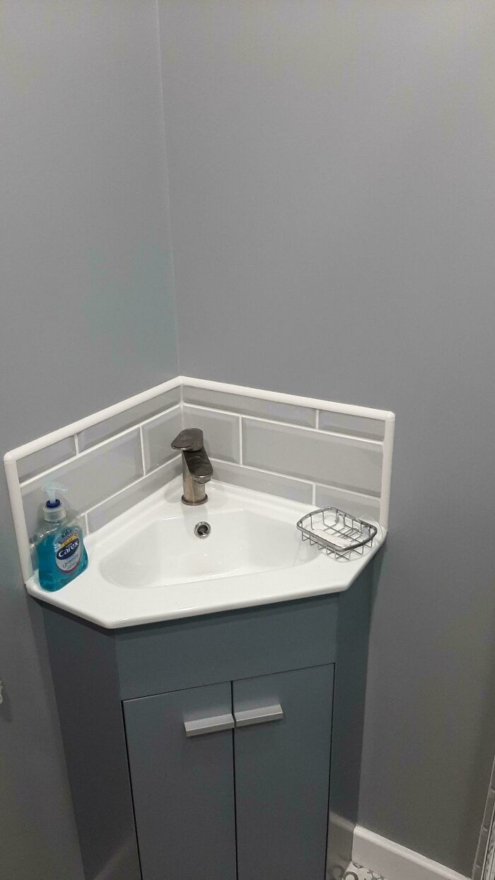 A modern corner sink with sleek gray tiles and a bronze faucet, part of a home renovation.