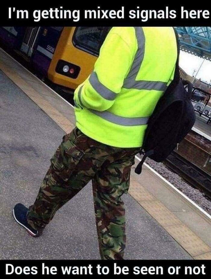 A person in a high-visibility vest and camouflage pants at a train station, creating a random joke about mixed signals.