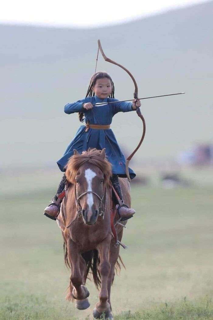 A young girl in traditional dress riding a horse and shooting a bow and arrow, a fascinating find.