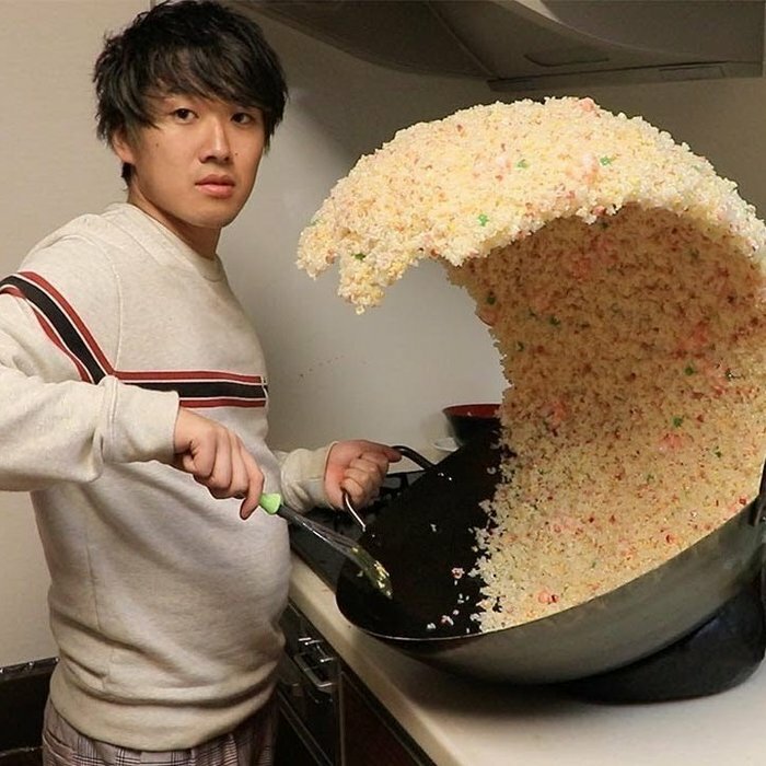 A man in a kitchen, performing a fascinating find: tossing a massive wave of fried rice from a wok.