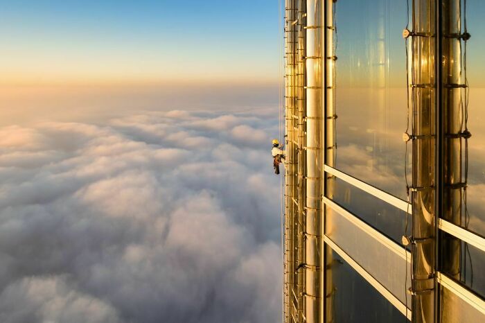A fascinating find: a window cleaner on a skyscraper above a sea of clouds at sunset.