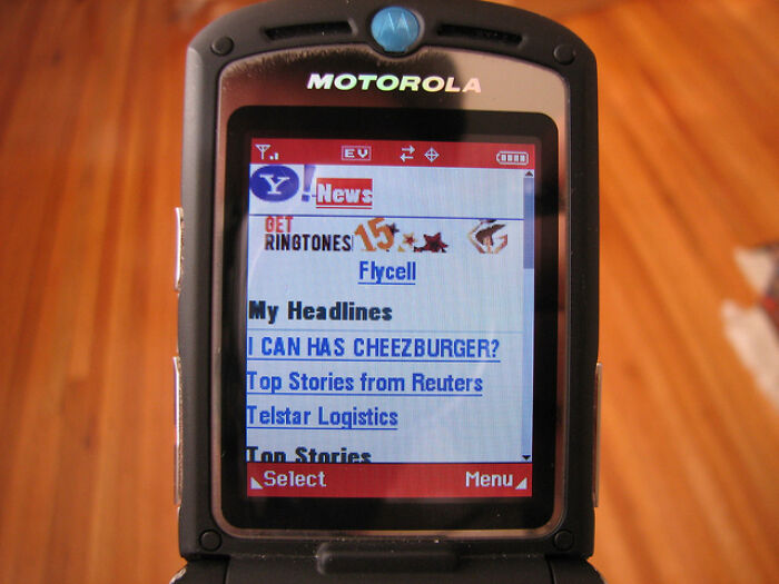 A Motorola flip phone displaying Yahoo! News headlines, including 'I CAN HAS CHEEZBURGER?', showcasing the old Internet.