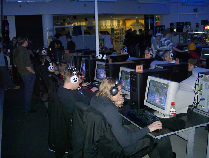 A chaotic pic of the old Internet with a room full of young people gaming on desktop computers at an internet cafe.