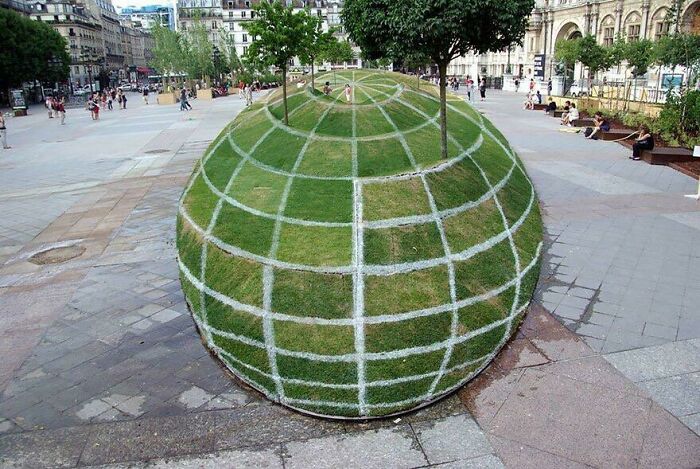 A fascinating find: a large spherical mound of grass with white grid lines, resembling a globe, in a city square.