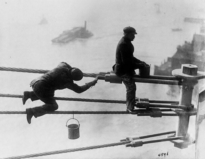 Two workers precariously painting high up on bridge cables, a fascinating find showing historical construction and brave work.