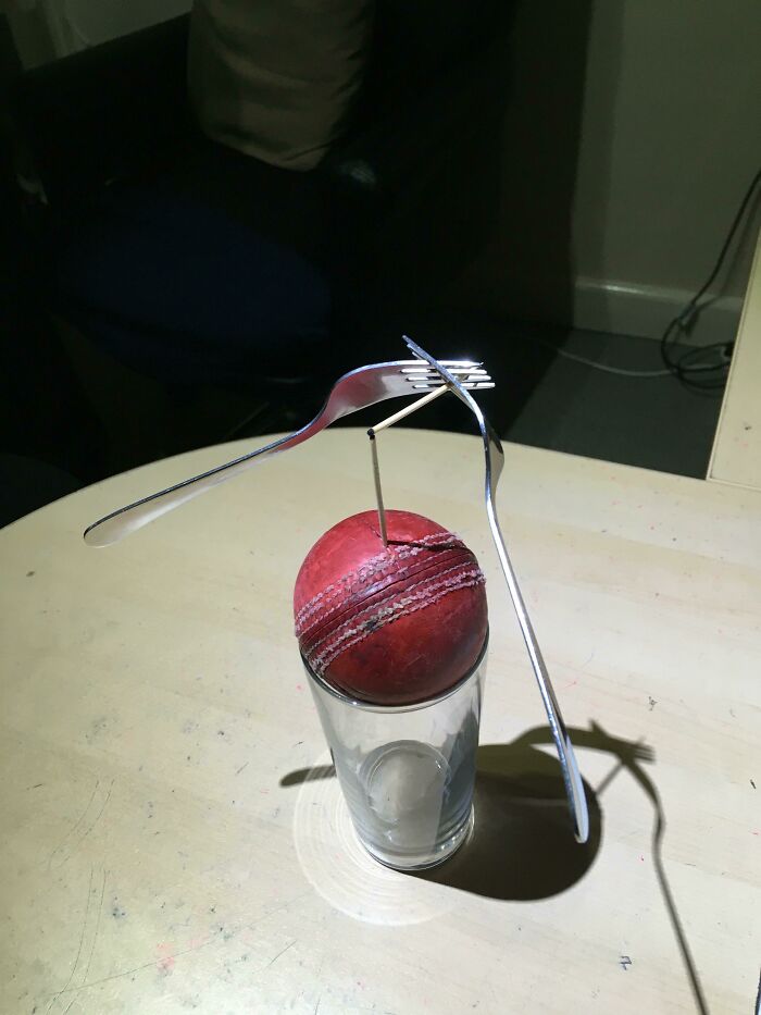 A red cricket ball balanced on a glass with two forks and a toothpick, a fascinating find demonstrating an unusual balance.