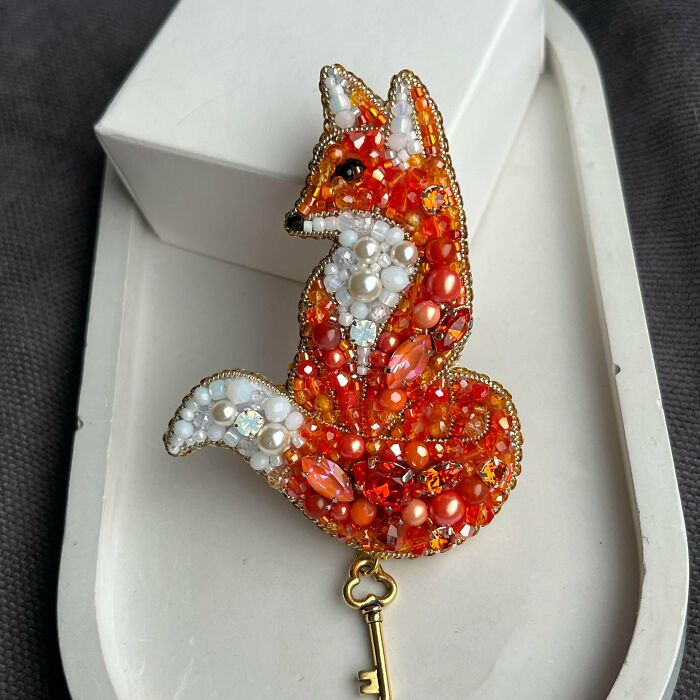 A dazzling handmade project: an intricately beaded fox brooch in shades of orange and white, holding a golden key.